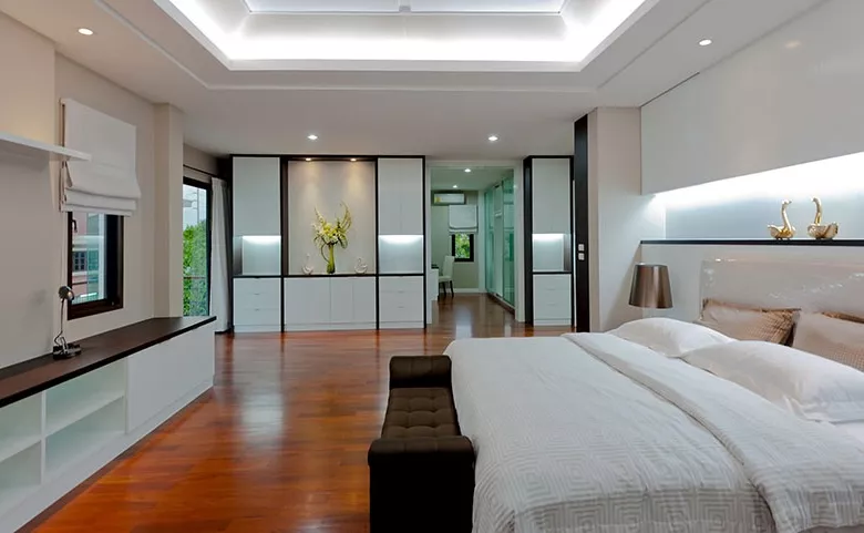 Modern bedroom with warm white LED strip lights installed behind the headboard and ceiling cove, creating a soft and luxurious ambient lighting effect.